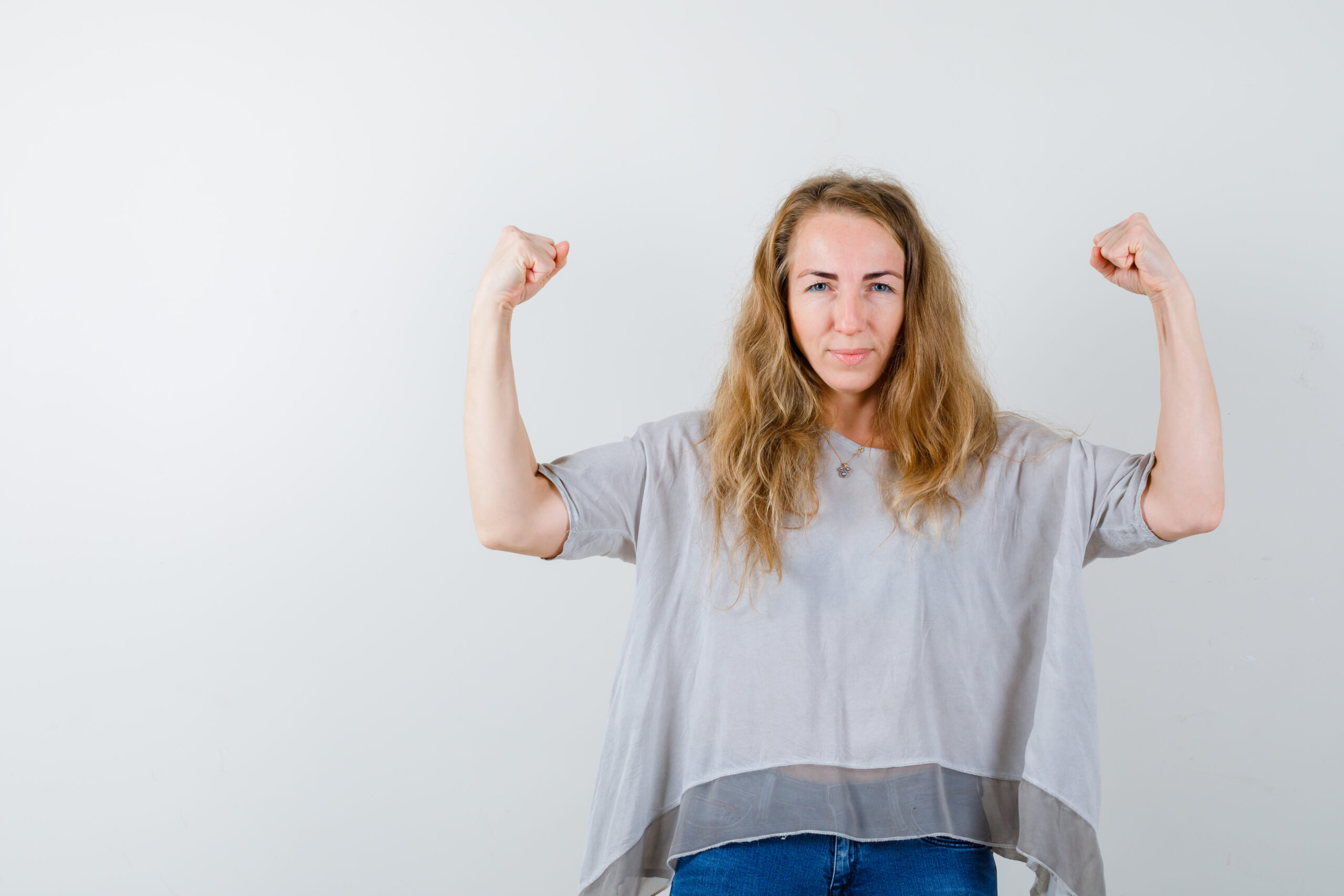 young lady showing winner gesture in blouse and looking proud , front view.